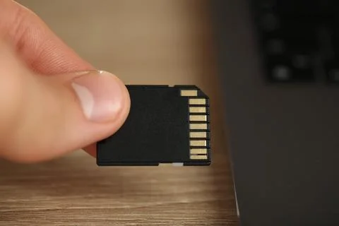 Man inserting SD memory card into laptop at wooden table, closeup Stock Photos
