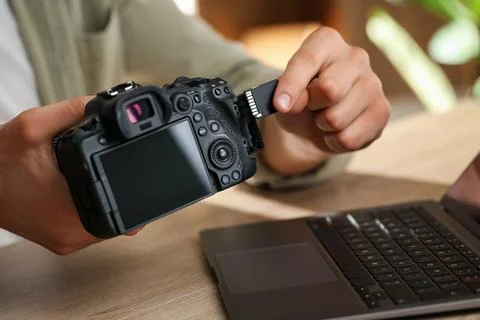 Man inserting SD memory card into photo camera at wooden table, closeup Stock Photos