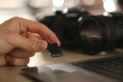 Man inserting SD memory card into laptop at wooden table indoors, closeup Stock Photos