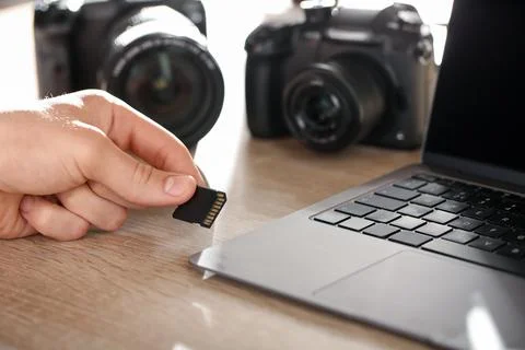 Man inserting SD memory card into laptop at wooden table indoors, closeup Foto stock