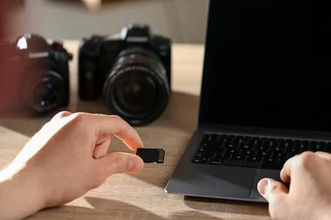 Man inserting SD memory card into laptop at wooden table indoors, closeup Foto stock