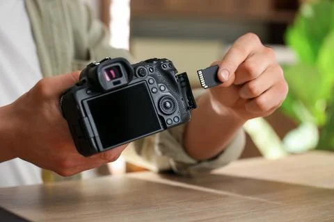 Man inserting SD memory card into photo camera at wooden table, closeup Foto stock