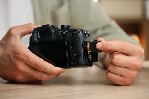 Man inserting SD memory card into photo camera at wooden table indoors, close Foto stock