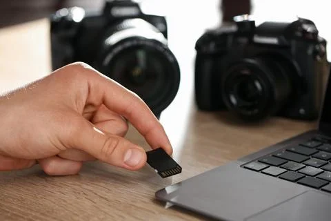 Man inserting SD memory card into laptop at wooden table indoors, closeup Foto stock