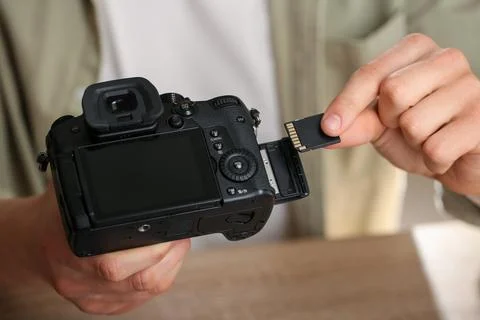 Man inserting SD memory card into photo camera at table, closeup Foto stock