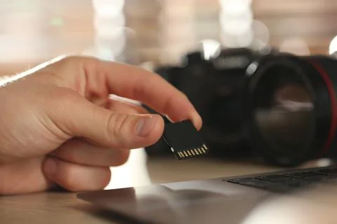 Man inserting SD memory card into laptop at table indoors, closeup Stock Photos