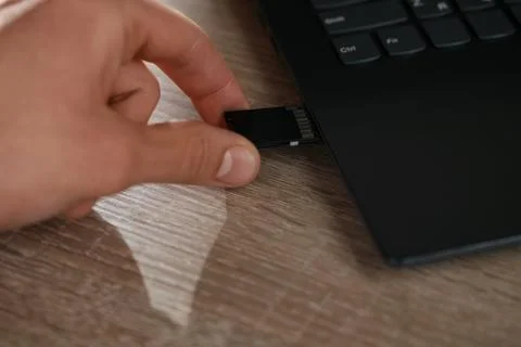Man inserting SD memory card into laptop at wooden table, closeup Stock Photos