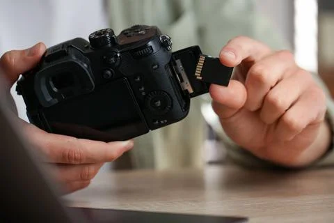 Man inserting SD memory card into photo camera at wooden table indoors, close Stock Photos