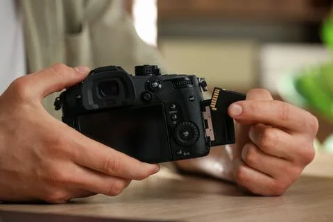 Man inserting SD memory card into photo camera at wooden table indoors, close Foto stock