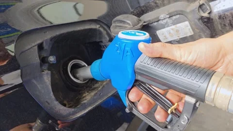 Man inserts a blue fuel nozzle into a car's tank at a gas station. 库存影片 340241593