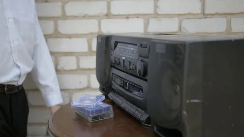 The man inserts the cassette into the old outmoded tape recorder and push play Video stock 69777840