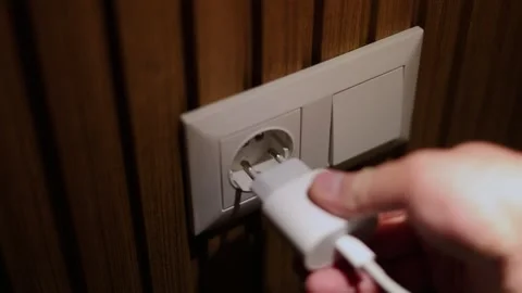 Man inserts charger plug of mobile phone from wall socket Stock Footage 329666956