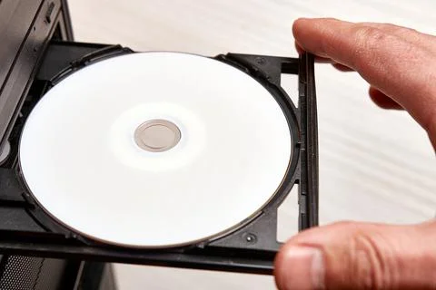A man inserts a disc into a disc player on his computer. Technologies of informa Stock Photos