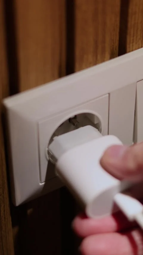 Man inserts mobile phone charger plug in white wall socket Stock Footage 311411706