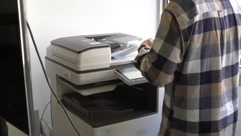 The man inserts paper into the printer with precision, signalling the 動画素材 235652488