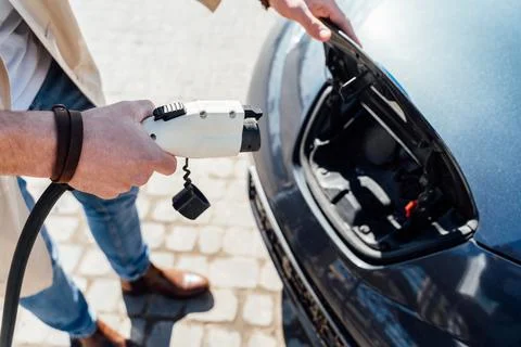 Man inserts plug of the charger into the socket of electric car close-up Stock Photos