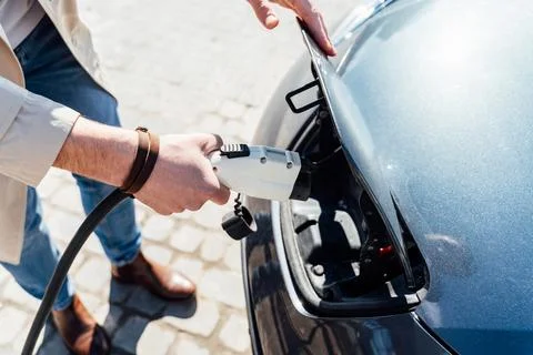 Man inserts plug of the charger into the socket of electric car close-up Stock Photos