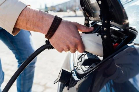 Man inserts plug of the charger into the socket of electric car close-up Stock Photos