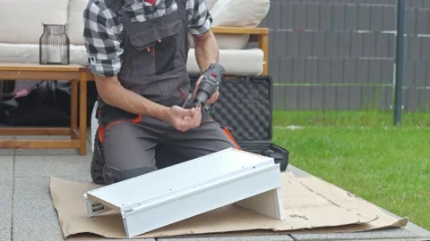 Man inserts screw and fastens white drawer unit with cordless drill Stock Footage 336580779
