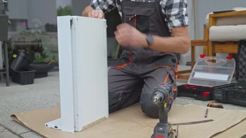 Man inserts screw into drawer panel and drives it with cordless drill Stock Footage 335703900