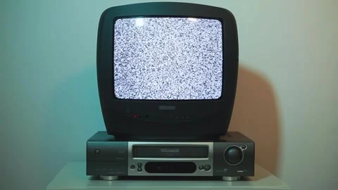 Man inserts a VHS tape into a video recorder with an old TV in a dark room. Vídeo Stock 258862539