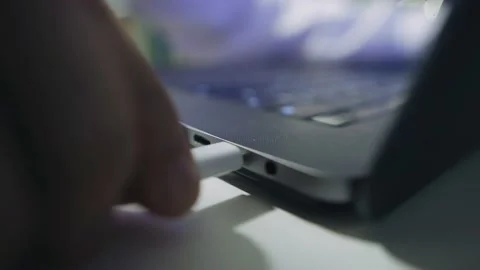 A man inserts a white plug of a wire into the port of a laptop Stock Footage 157501634
