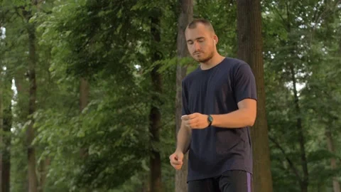 Man inserts wireless headphones in the park and listens to music Stock Footage 91498627