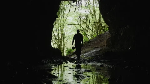 Man inside a cave against jungle rainforest. Scenic view of a man walking in a Stock Footage 204865943