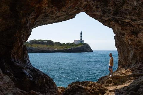 Man inside cave, view Lighthouse Portocolom in Mallorca. Stock Photos