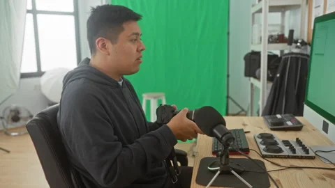 Man inspecting camera while seated at desk with microphone and monitor in a.. Stock Footage 347800660