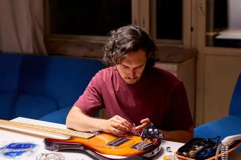Man inspecting small guitar electronics component at cluttered workbench in dim Fotos de archivo