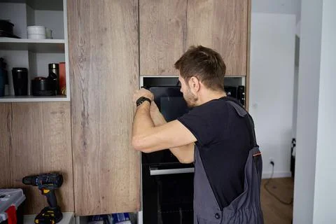 Man installing built in microwave oven in kitchen cabinet Stock Photos