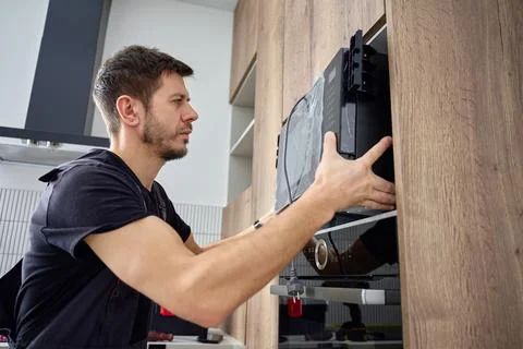 Man installing built in microwave oven in modern kitchen cabimet Stock Photos