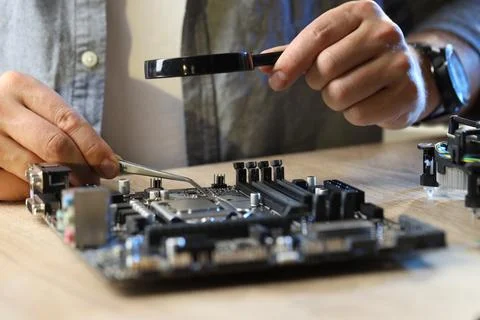 Man installing computer chip onto motherboard at wooden table, closeup Stock Photos