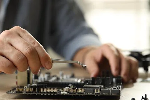 Man installing computer chip onto motherboard at wooden table, closeup Stock-Fotos