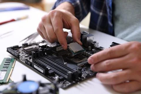Man installing computer chip onto motherboard at white table, closeup Stock-Fotos