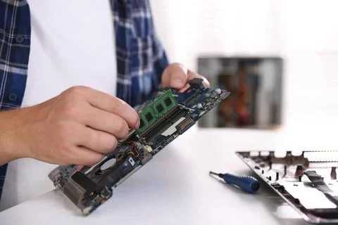 Man installing computer chip onto motherboard at white table, closeup Stock-Fotos