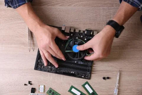 Man installing computer chip onto motherboard at wooden table, top view Stock-Fotos