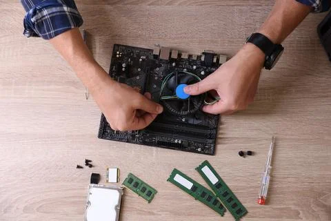 Man installing computer chip onto motherboard at wooden table, top view Stock Photos