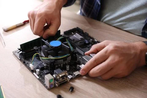 Man installing computer chip onto motherboard at wooden table, closeup Stock-Fotos