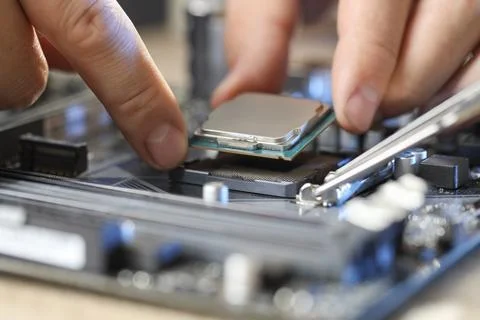Man installing computer chip onto motherboard at table, closeup Stock-Fotos