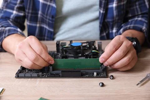 Man installing computer chip onto motherboard at wooden table, closeup Stock-Fotos