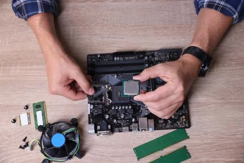 Man installing computer chip onto motherboard at wooden table, top view Stock-Fotos