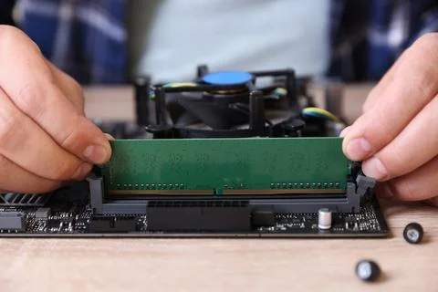 Man installing computer chip onto motherboard at wooden table, closeup Stock-Fotos