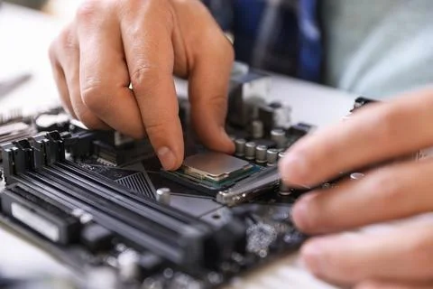 Man installing computer chip onto motherboard at white table, closeup Foto stock