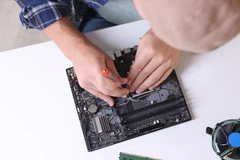Man installing computer chip onto motherboard at white table, top view Stock-Fotos