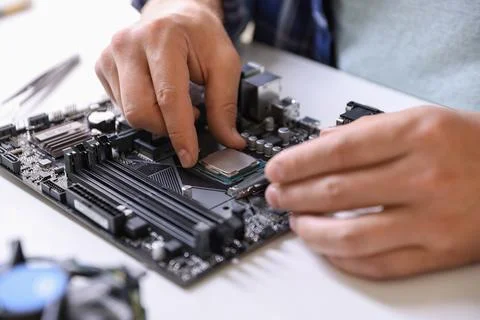 Man installing computer chip onto motherboard at white table, closeup Stock-Fotos