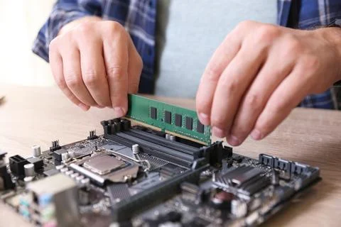 Man installing computer chip onto motherboard at wooden table, closeup Stock-Fotos