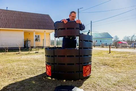Man installing factory made panel compost bin near rural house. Фото