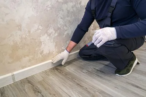Man installing new baseboard molding on wall with laminate flooring. Worker.. Stock Photos